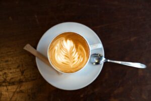 Top-down image of a cappuccino with latte art on a wooden table, served with spoon and sugar.