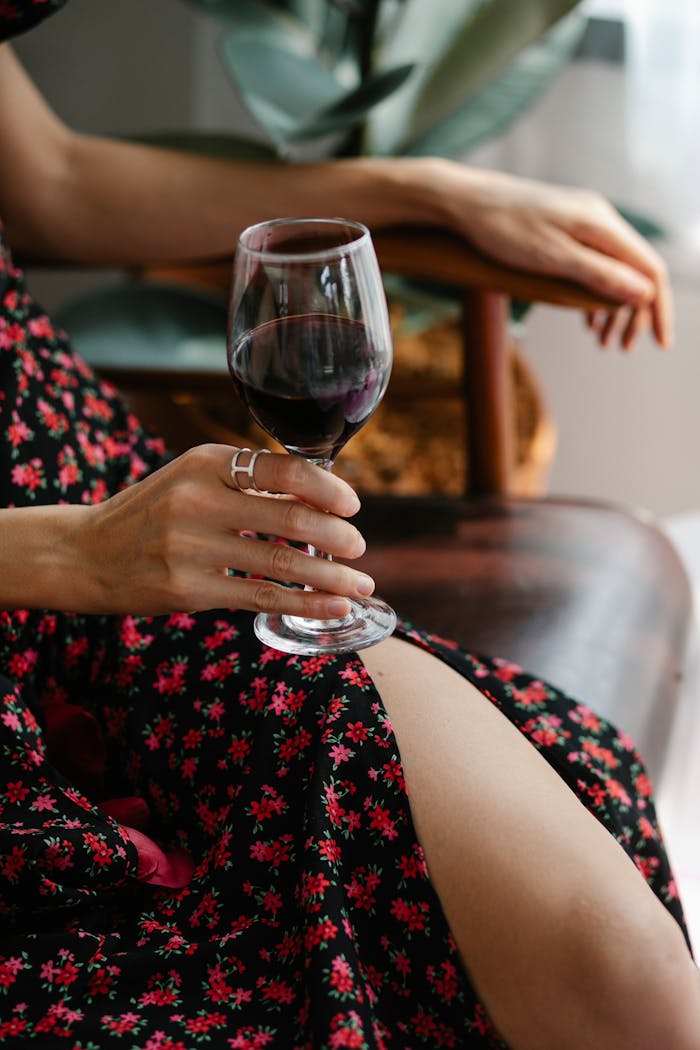 A woman in a floral dress holding a wine glass inside a cozy room.